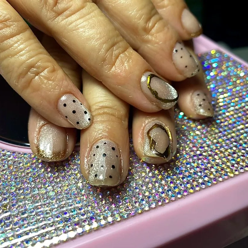 Nude nails with black dots and hand-painted gold lines, on a crystal base